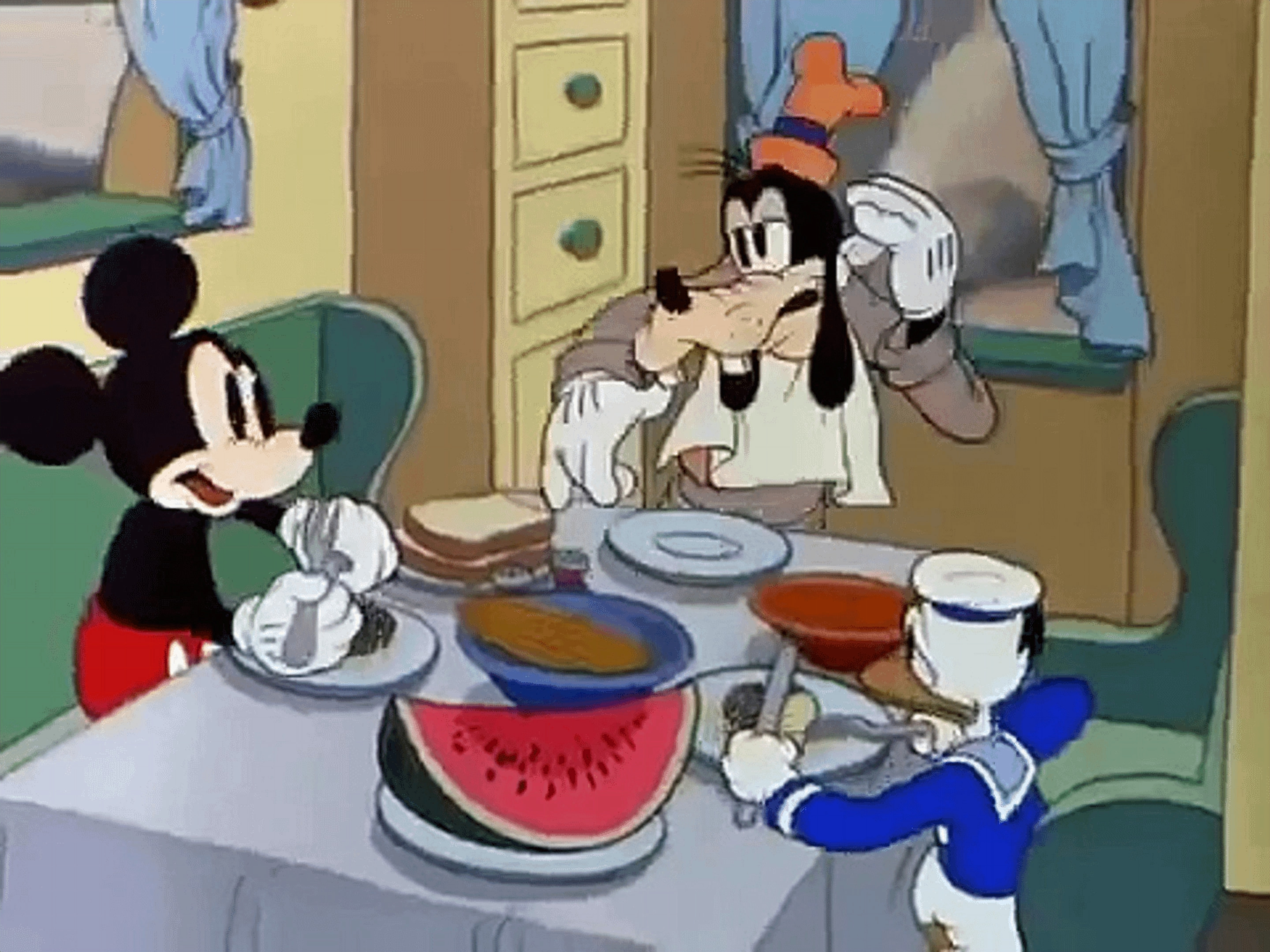 Mickey, Goofy, and Donald at a table while Goofy asks who is driving